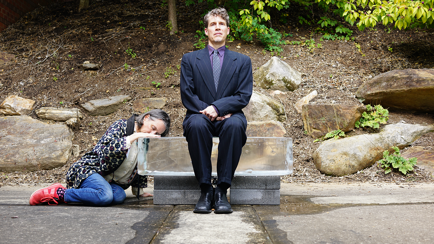 All That Is Solid Melts Into Air, 2025, 40 x 18 x 20 bench (300 lb ice block)<br><br>Describing how the bourgeoisie preserve control Karl Marx wrote “all that is solid melts into air.” New becomes old before it can solidify. People constantly experience changing realities and truths. Uncertainty cloaks the facts. Dressed in a suit and tie, similar to John Cage in his 1959 “Water Walk,” I sit on a bench of ice. ReViewing Black Mountain College Conference attendees partake too. Accompanying the performance, a speaker broadcasts the sound of melting ice. In “Water Walk,” Cage created music from sounds of overlooked everyday water related items, while “All That Is Solid Melts Into Air’s” soundscape makes audible the almost imperceptible melody of melting ice. Wet bottoms from the melting ice imprint and remind us of our experience of unrelenting change and ambiguity.